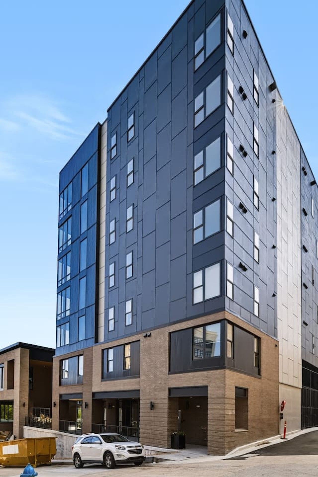 A multi-story building with a modern architectural design, featuring a mix of glass and brick facades, and a car parked in front.