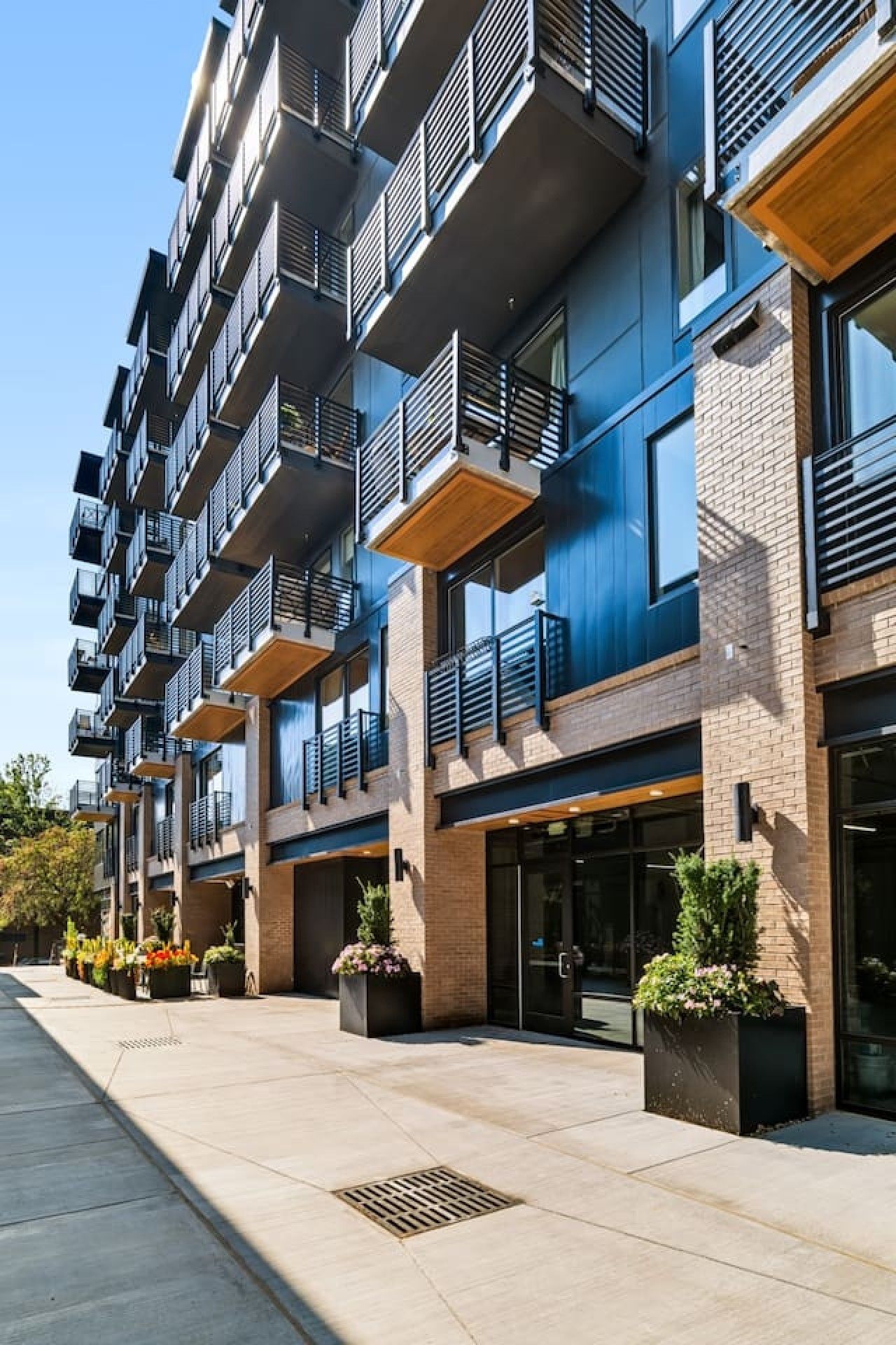 A modern multi-story residential building with balconies, large windows, and outdoor planters.