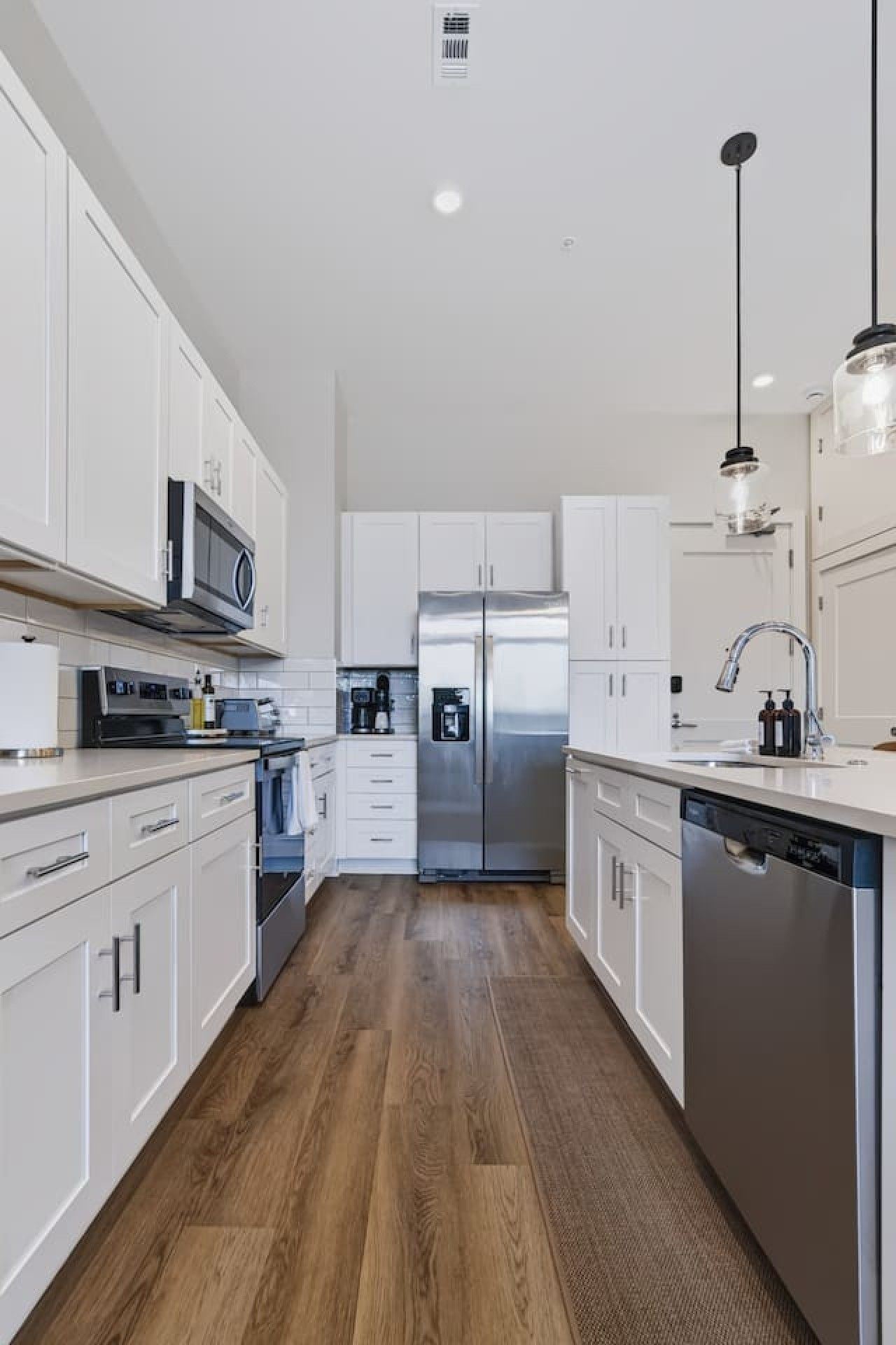 A modern kitchen with white cabinetry, stainless steel appliances, and a wooden floor.
