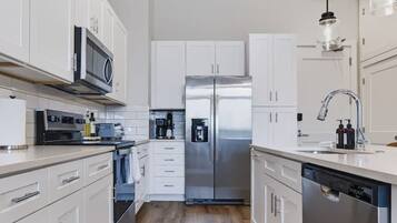 A modern kitchen with white cabinetry, stainless steel appliances, and a wooden floor.