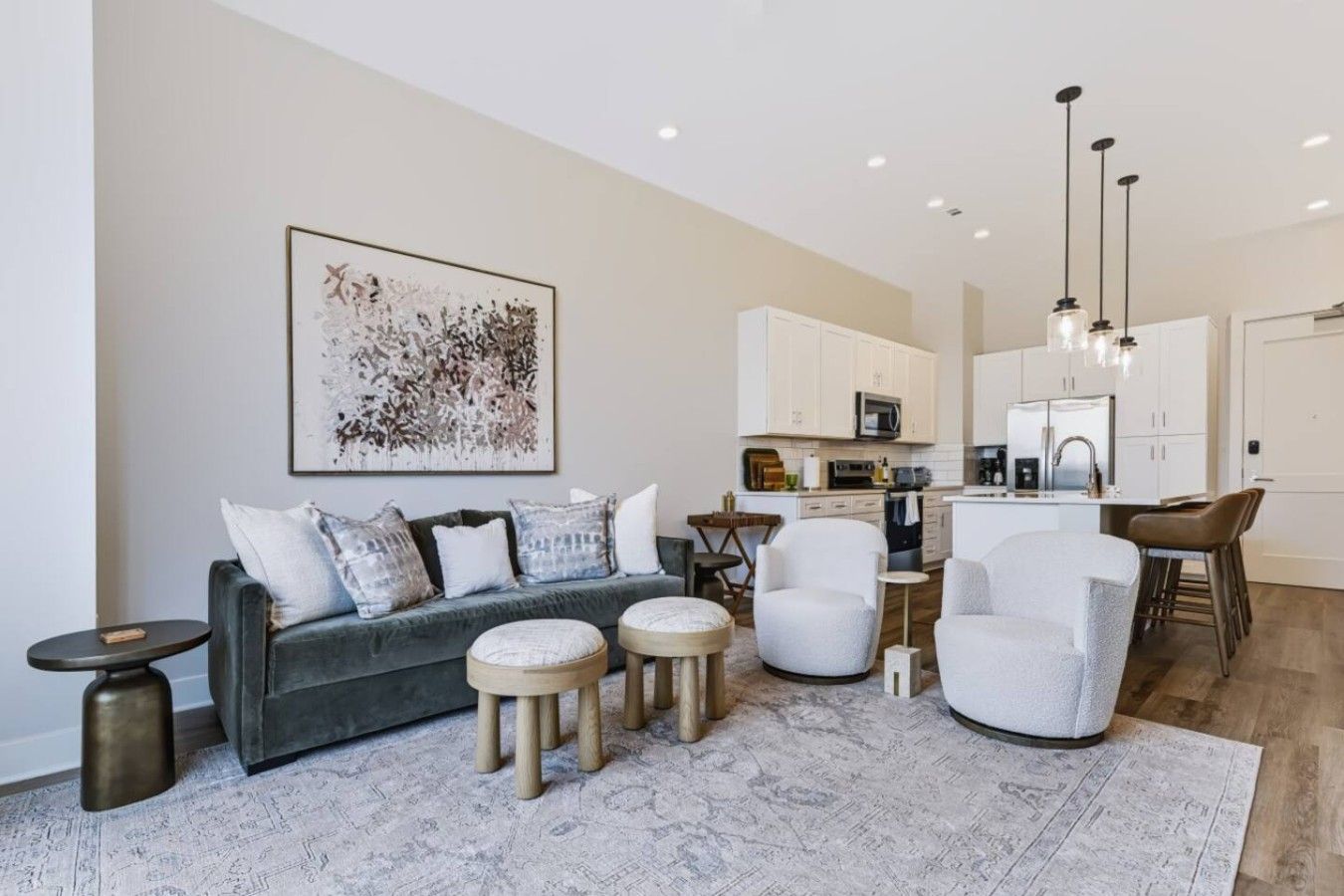 A modern living room with a grey sofa, white armchairs, a coffee table, and a kitchen in the background.