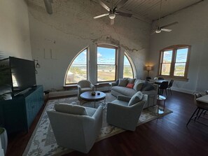 A spacious living room with a large television, comfortable seating, and large windows offering a view of the landscape. - City Views & Comfort | Heart of Downtown Knoxville (Knoxville)