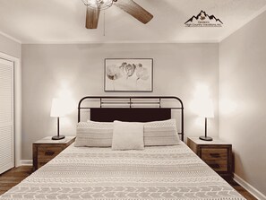 A bedroom with a bed, two bedside tables, a ceiling fan, a wall-mounted artwork, and a logo on the wall. - Walk to Slopes from Sugar Ski (Sugar Mountain)
