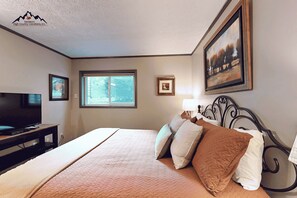 Quarto com cama, televisão, janela e quadros na parede.