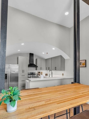 Una cucina moderna con mobili bianchi, un frigorifero in acciaio inossidabile e un tavolo da pranzo in legno con una pianta in vaso.