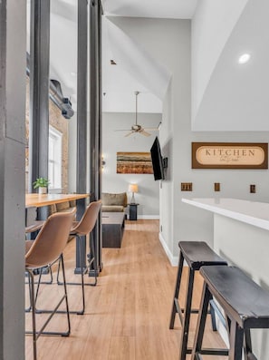 Una cucina moderna con un cartello 'KITCHEN let's eat', pavimento in legno e un'area pranzo con sedie e tavolo.
