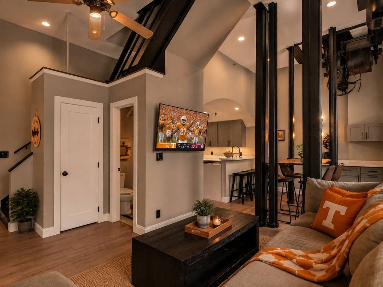Un salon moderne avec un téléviseur à écran plat, une table basse et un canapé agrémenté d’un grand coussin en forme de lettre.