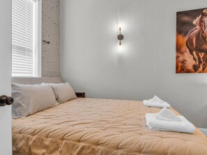 Un dormitorio con cama, almohadas, una lámpara de pared y un cuadro.