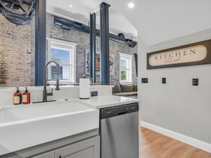 A modern kitchen with a brick wall, stainless steel appliances, and a sign that reads 'KITCHEN let's eat.' - The Jackson Gem | Steps to Knoxville’s Old City (Knoxville)
