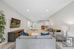 A spacious living area with a sofa, a coffee table, and a TV mounted on the wall. - 6BR Near Disney Private Pool, spa & Loft (Kissimmee)