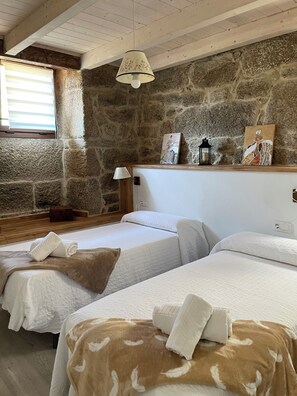 A room with two beds, a stone wall, a wooden ceiling, and a hanging lamp.