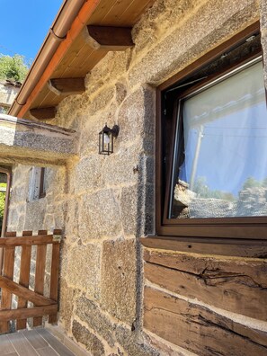 A stone exterior with a wooden bench, a window with a view, and a wall-mounted light fixture.