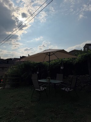 Une terrasse extérieure avec une table et des chaises, un grand parasol et un mur en pierre.