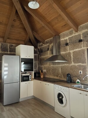 Une cuisine compacte dotée d’un four, d’un micro-ondes et d’un lave-linge intégrés, de murs en pierre et de poutres en bois.
