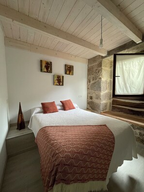 A bedroom with a bed, a stone wall, and a window. - As Fontaiñas (Berán)