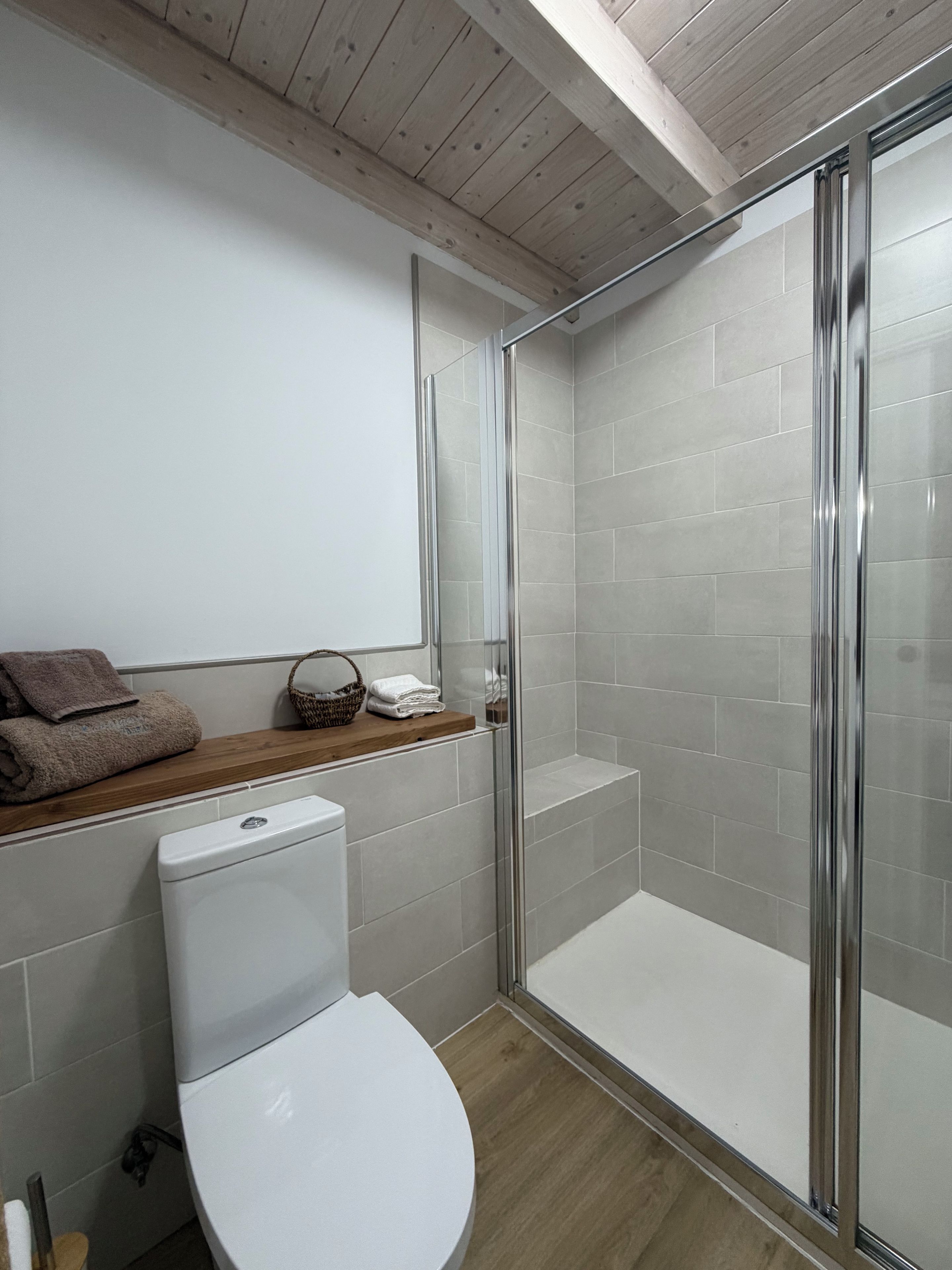 Een moderne badkamer met een douchecabine van glas, een toilet en een houten wastafelmeubel met handdoeken.
