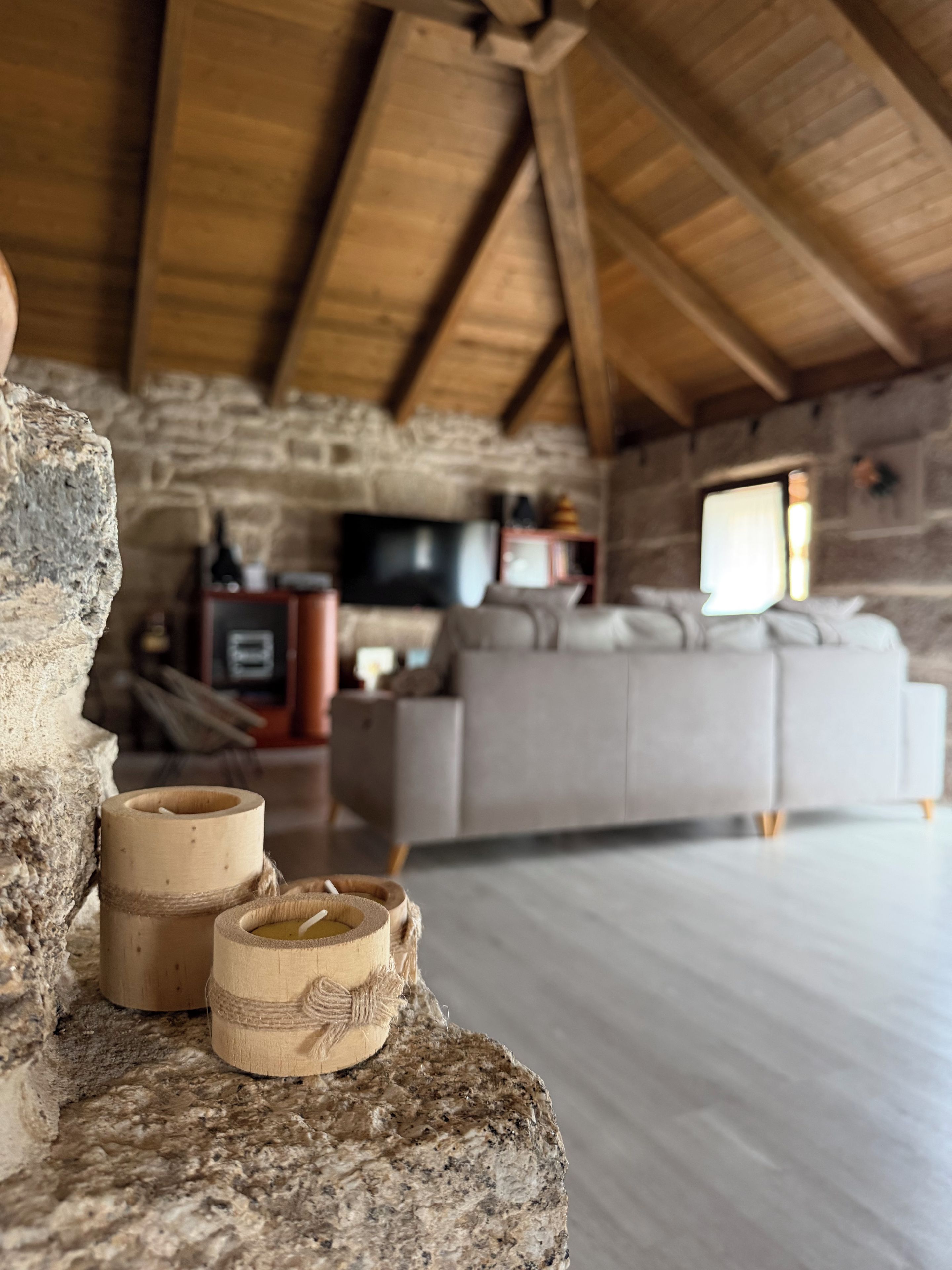 Un interior rústico con pared de piedra, vigas de madera, chimenea de piedra, un sofá y un televisor.