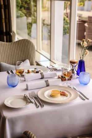 A table set for dining with plates, cutlery, and glasses, and a vase with flowers. - Airds Hotel (Appin)