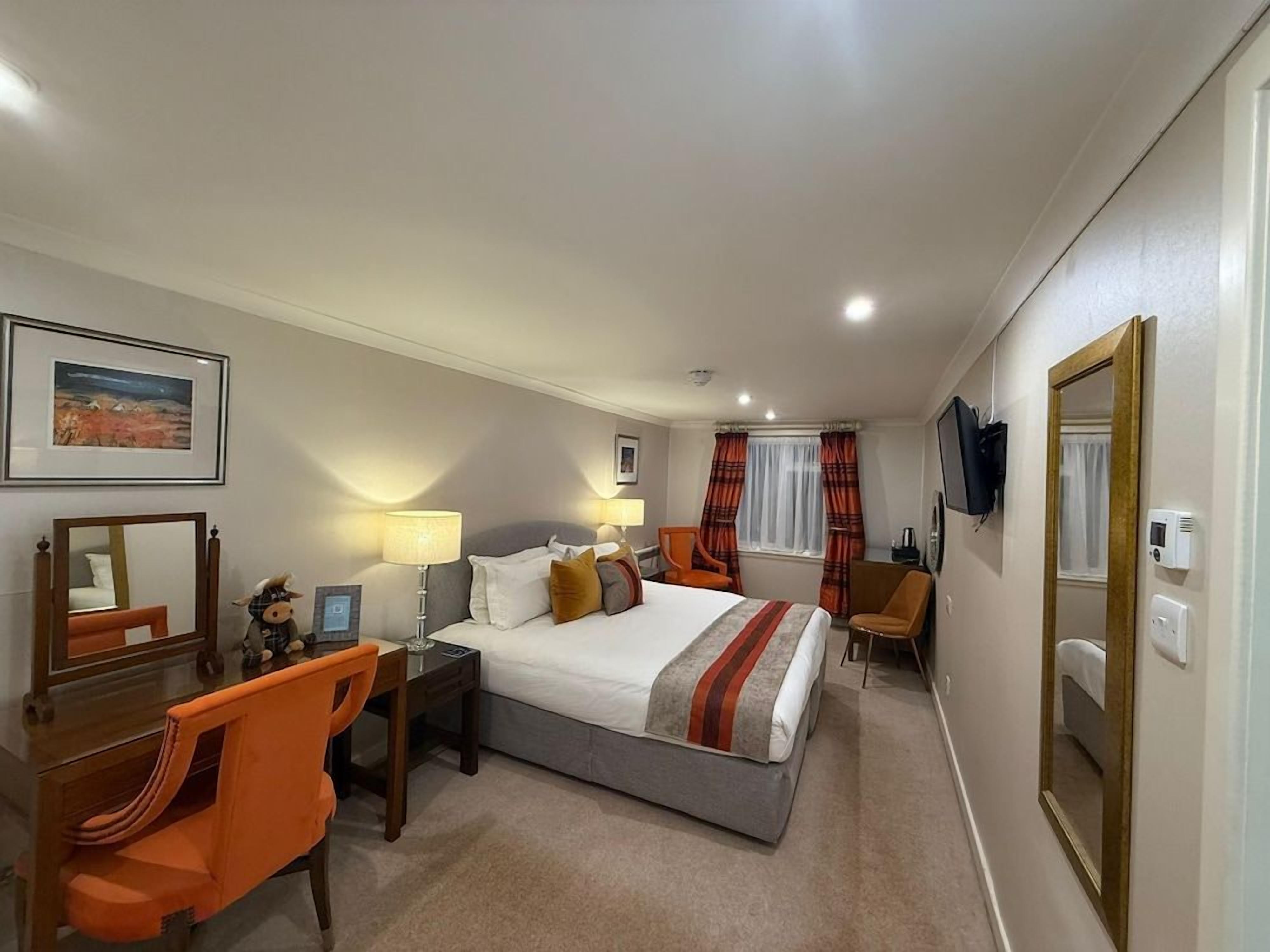 A hotel room with a bed, desk, chair, and a television.