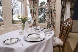 Una mesa de comedor decorada con mantel blanco, platos azul y blanco, cubiertos y un jarrón con flores blancas.