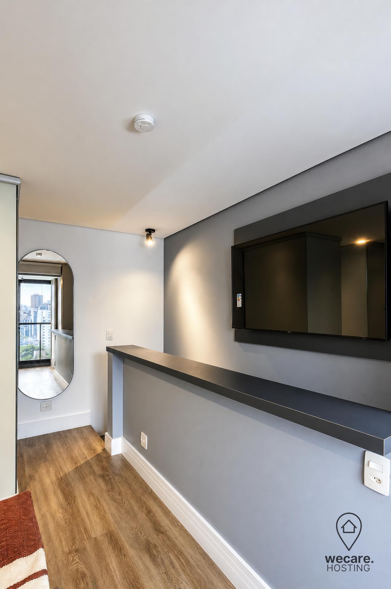 A modern hallway with a built-in TV, a round mirror, and a view of the city through a window.
