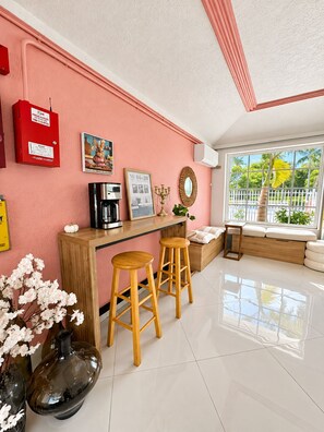 Eine moderne Küche mit einer rosafarbenen Wand, einer Holztresore und zwei Barhocker, sowie einer Kaffeemaschine.