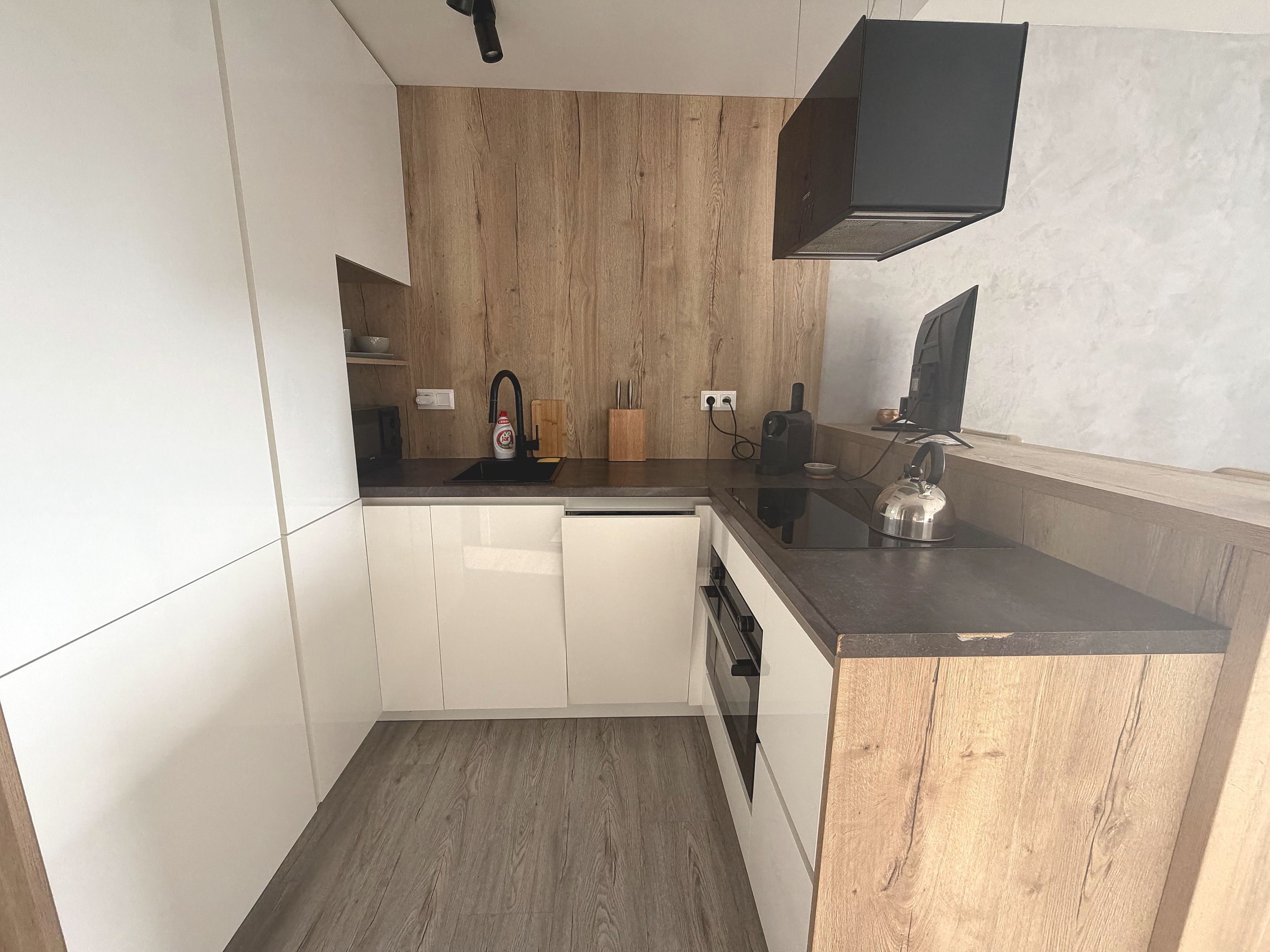 A compact kitchen with white cabinets, a wooden backsplash, and a black countertop.