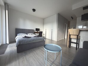 Un dormitorio moderno con una cama, un escritorio, una silla y una kitchenette.