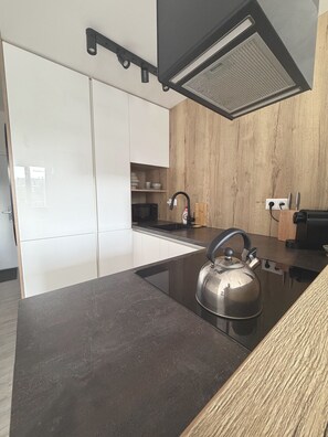 Una cocina moderna con encimera negra, hervidor de acero inoxidable y paneles de madera en la pared.