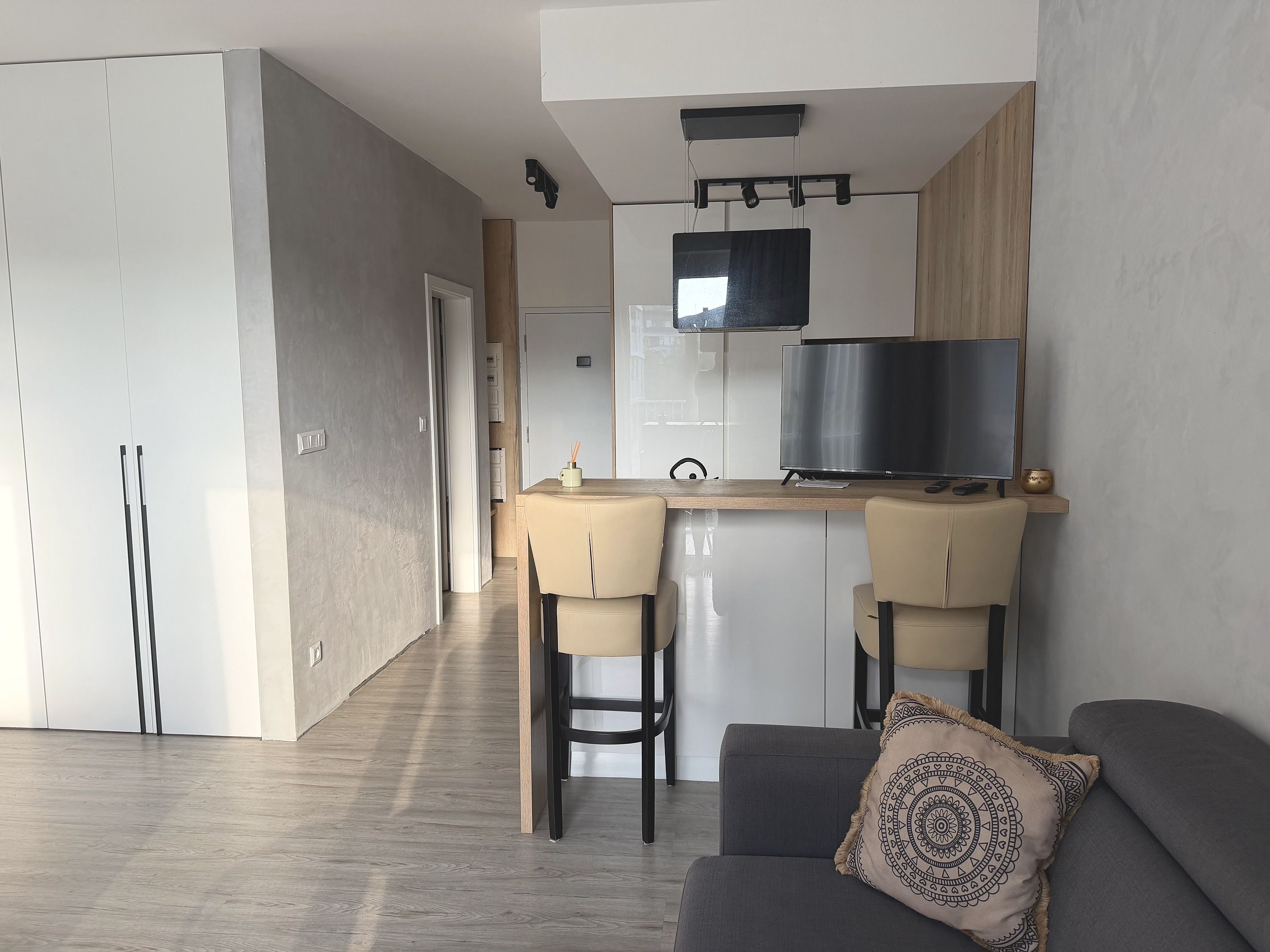 A modern kitchen with a flat-screen TV, a dining area with two chairs, and a sofa with a patterned cushion.