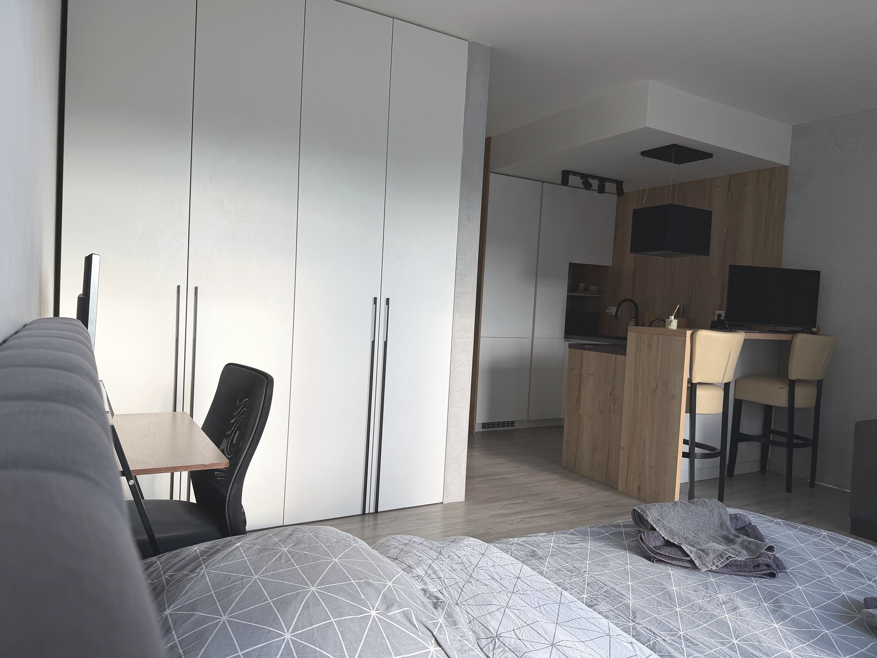 Un dormitori modern amb un llit, escriptori i una zona de cuina petita.