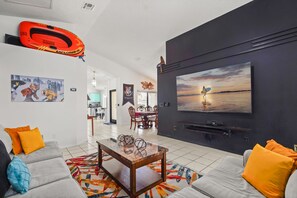 Uma sala de estar com televisão de tela plana, sofá, mesa de centro e tapete colorido.