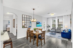 A dining area with a wooden table and chairs, a chandelier, and a view of the living room. - Near Epic! 3 BD/ 2 BA/ Vista Cay (4862-110 CA) (Orlando)