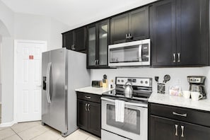 A modern kitchen with dark cabinets, a stainless steel refrigerator, a microwave, a stove, and a coffee maker. - Near Epic! 3 BD/ 2 BA/ Vista Cay (4862-110 CA) (Orlando)