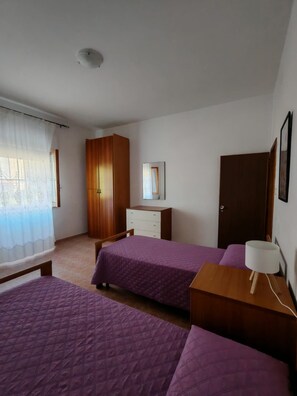 Une chambre avec deux lits, une armoire en bois, une commode, un miroir et une table de chevet avec une lampe.