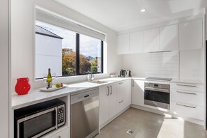 A modern kitchen with a large window, stainless steel appliances, and a minimalist design. - Town House Hagley Park - Christchurch Holiday Home (Christchurch)