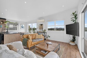 A modern living space with a sofa, coffee table, and a television. - Sunset Vista - Mangawhai Heads Holiday Home (Mangawhai)