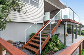 Eine moderne Außentreppe führt zu einem Glasbalkon, umgeben von viel Grün und einer Holzterrasse.