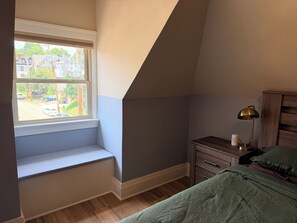 A bedroom with a window, a bedside table, a lamp, and a bed.