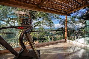 A treadmill with a control panel, a glass railing, and a view of a lush landscape. - Casa La Torre (Porto Seguro)