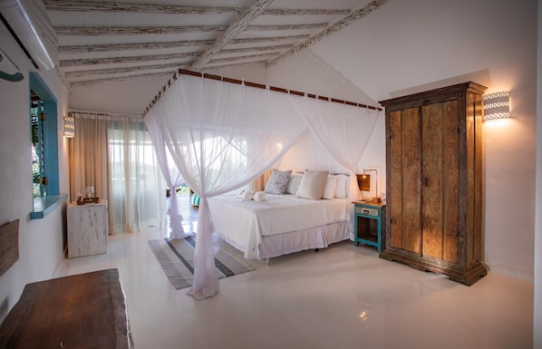 A bedroom with a canopy bed, a wooden wardrobe, and a nightstand with a lamp. - Casa La Torre (Porto Seguro)