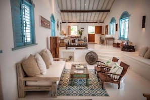 A spacious living area with a sofa, coffee table, and chairs, a patterned rug, and a kitchen in the background. - Casa La Torre (Porto Seguro)