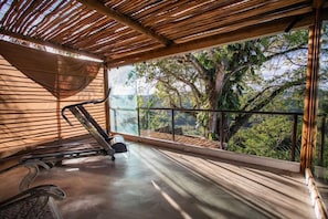 A gym with a treadmill, a stationary bike, and a rowing machine, overlooking a lush green landscape. - Casa La Torre (Porto Seguro)