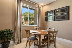 A dining area with a round wooden table, four chairs, a potted plant, and a window with curtains. - 4 Suites Near Disney Balcony & Covered Patio (Kissimmee)