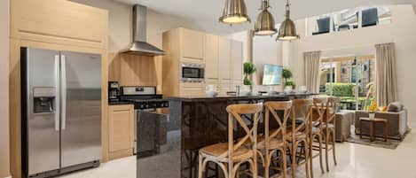 A modern kitchen with stainless steel appliances, a central island with bar stools, and pendant lighting.