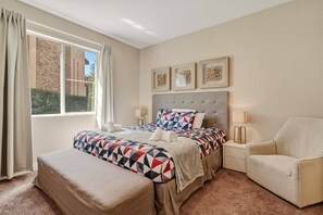 A hotel room with a bed, a chair, a window with curtains, and artwork on the wall. - 4 Suites Near Disney Balcony & Covered Patio (Kissimmee)