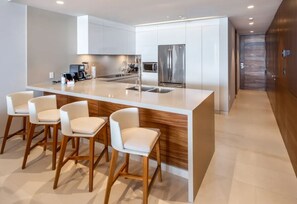 A modern kitchen with a central island, bar stools, stainless steel appliances, and a wooden accent wall. - New Year's Week in Los Cabos: Beachfront Luxury Suite -sleeps up to 4- Two Baths (B.C.S.)