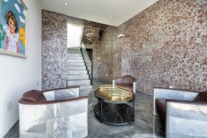 A modern interior with a staircase, two leather chairs, a glass coffee table, and a textured wall. - Viewmont Skyterrace By Alora Reserve (Los Angeles)