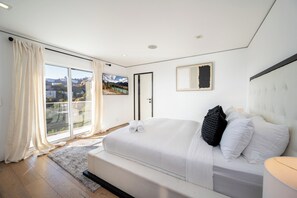 A modern bedroom with a large bed, a view of a mountainous landscape through a sliding door, and a framed picture on the wall. - Viewmont Skyterrace By Alora Reserve (Los Angeles)