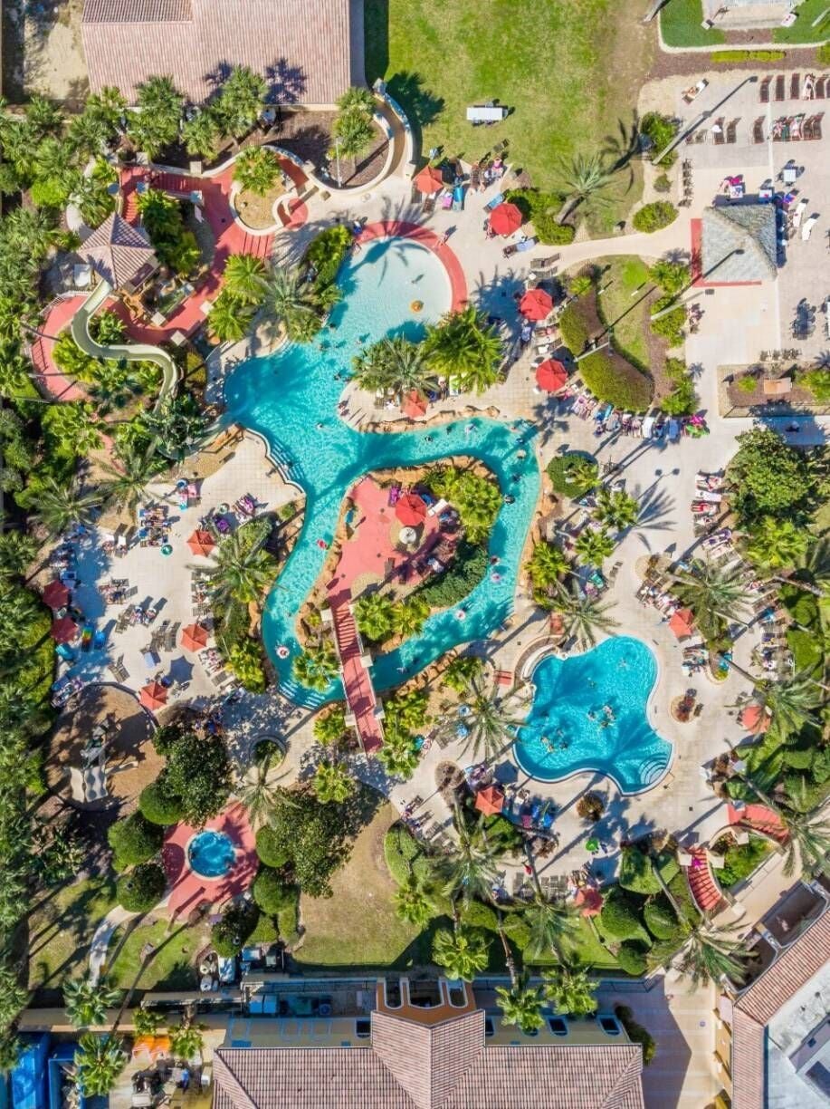 An aerial view of a resort with multiple swimming pools, sun loungers, and palm trees.